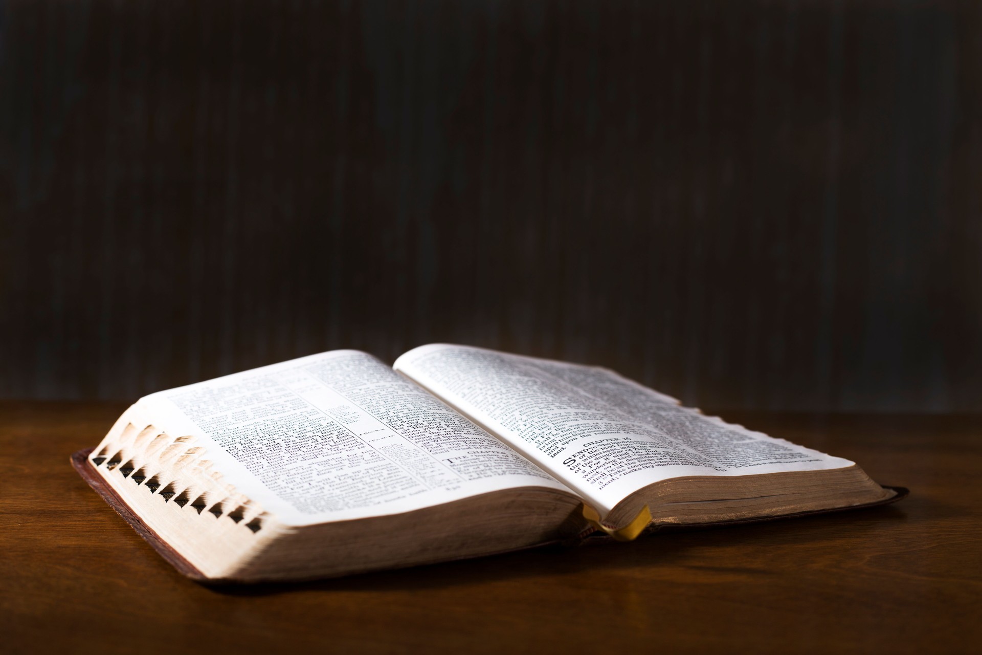 Open book or Bible on highly polished wood table.  Black background.